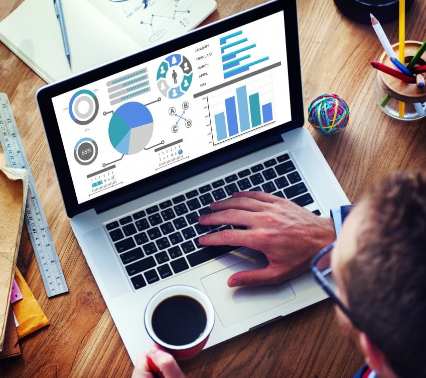 Man at his laptop looking at graphs with a cup of coffee in his hand.
