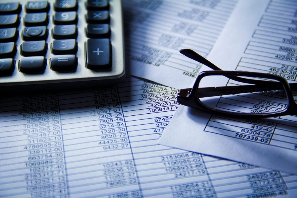 Glasses, Excel spreadsheets and a calculator spread out on a desk.